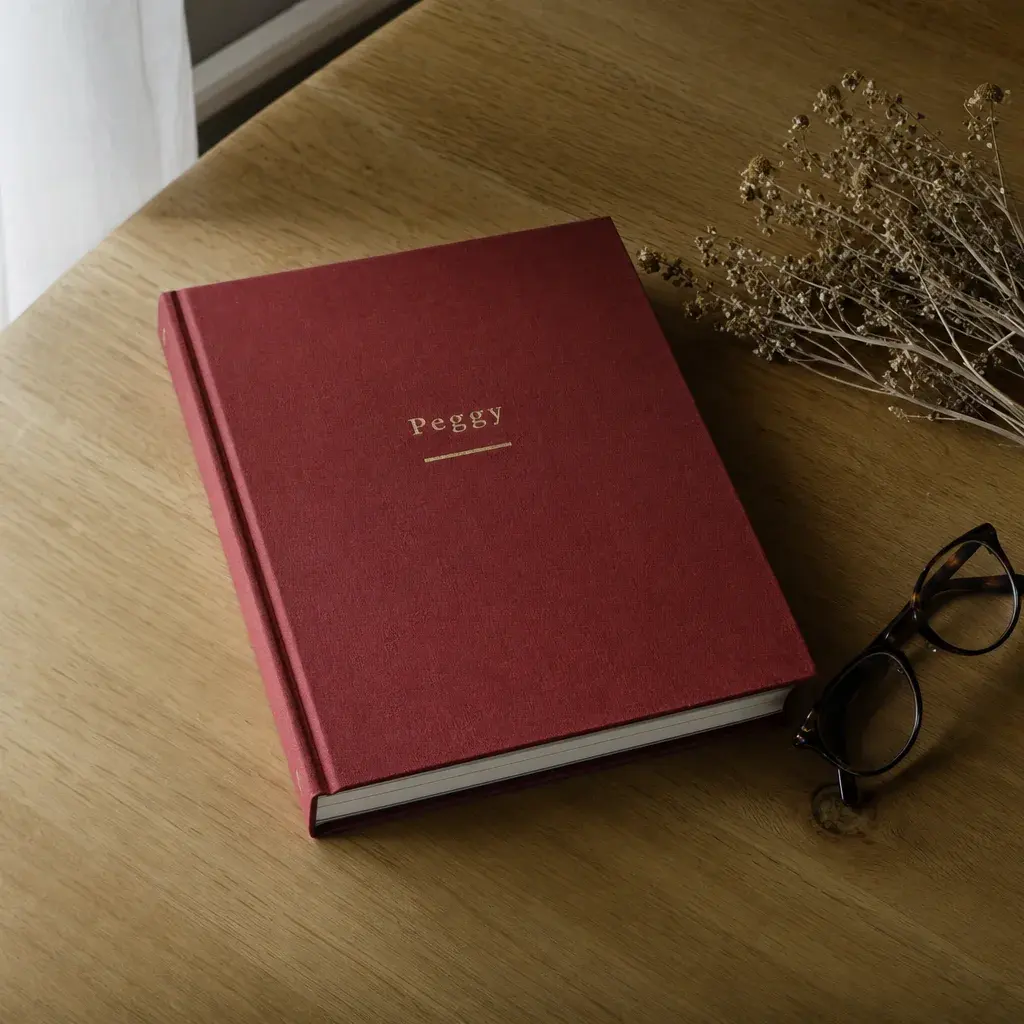 The hardcover memoir with a deep red linen cover on a table