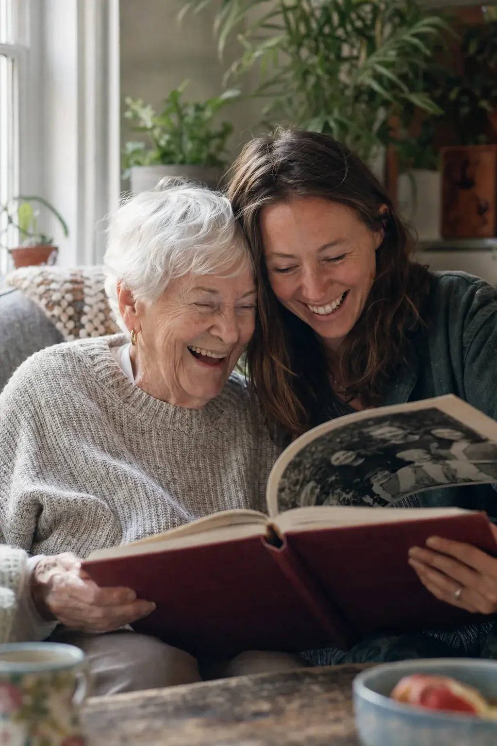 A grandmother and her granddaughter laughing over a hardcover memoir on the sofa