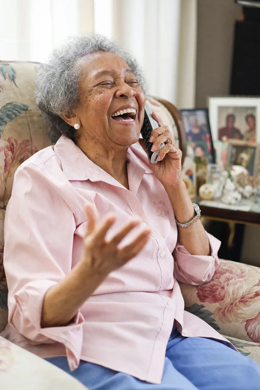 An older woman laughing during a phone call in her armchair